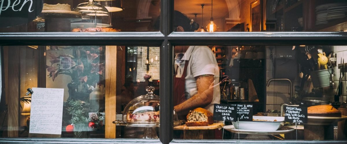 Warm bakery scene in London through window showcasing pastries and chef at work.